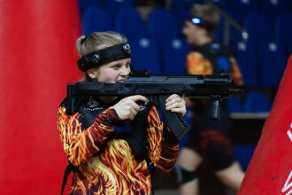 Девушка LASERWAR прицеливается из-за красного укрытия.
